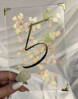 Număr de masă pentru nuntă din plexiglas transparent cu flori uscate și număr în relief auriu, design elegant realizat de Diandra Events