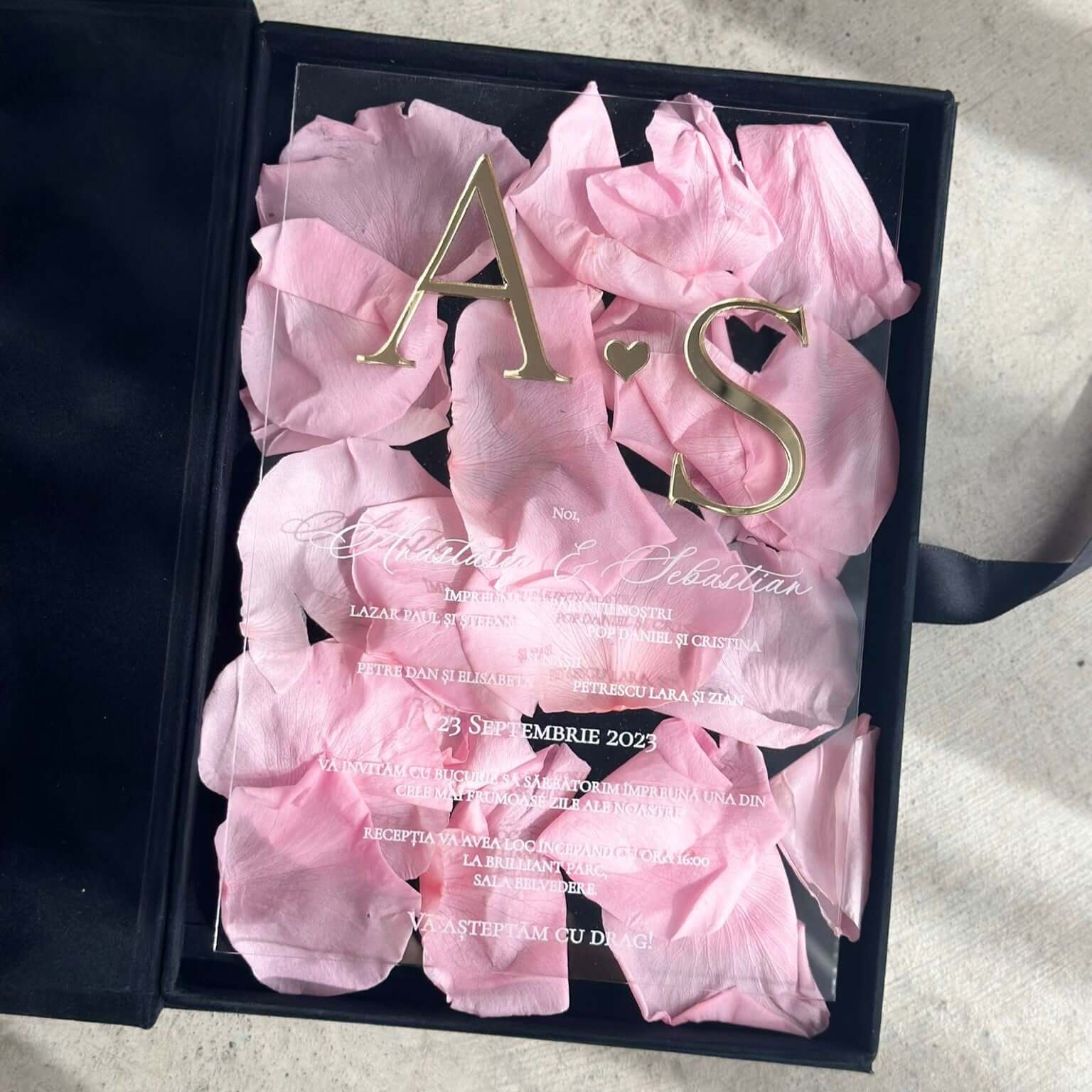 Model premium invitație de nuntă acrilică personalizată, decorată cu petale roz și litere aurii, ideală pentru evenimente elegante