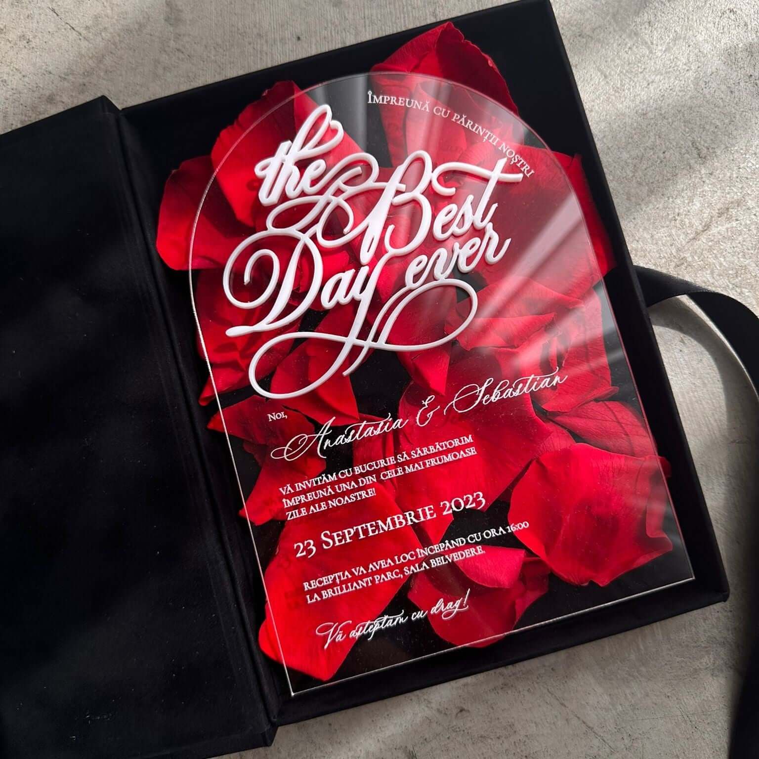 Invitație de nuntă acrilică transparentă cu design elegant și petale roșii de trandafir, prezentată într-o cutie de catifea neagră